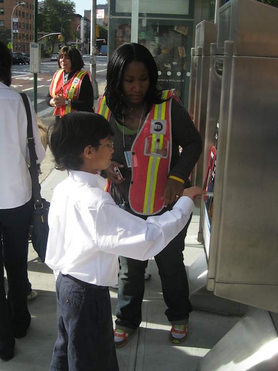 An MTA employee helps a school-bound child learn how to pay his bus fare before boarding. He didn't have any trouble. Photo: Noah Kazis.