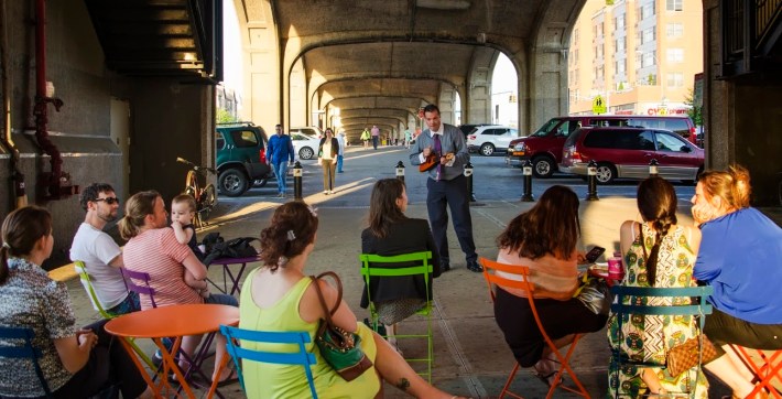 Roberto Buscarsi plays during Make Music New York at 40th Street and Queens Boulevard. The parking in the background will remain, but space beneath the elevated 7 train in Sunnyside is set for some plaza improvements. Photo courtesy Sunnyside Shines BID