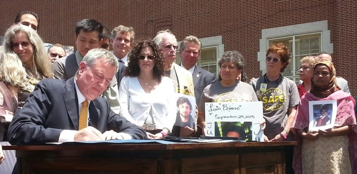 Mayor de Blasio signs 11 traffic safety bills this morning at PS 152 in Queens, surrounded by families of traffic violence victims. Photo: Stephen Miller