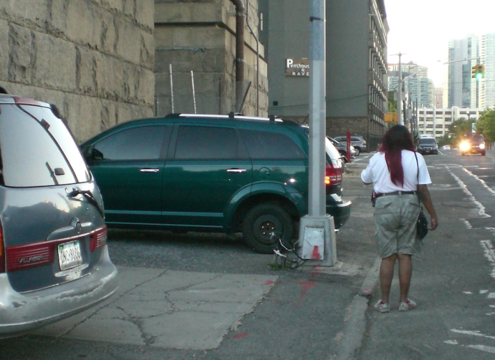 Around the corner, on Vernon Boulevard, illegally-parked cars continue to force pedestrians into oncoming traffic. Photo: Ray Normandeau