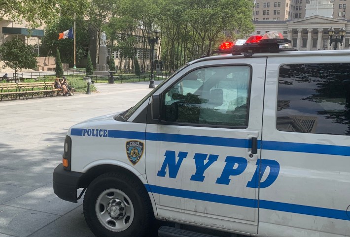 The statue is in the background, under the watchful eyes of the police officers in the van.