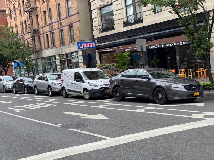 The line of illegally parked cars includes a florist shop truck that is benefitting from the NYPD's lack of enforcement against its own officers' parking in a left-turn bay. Photo: Streetsblog