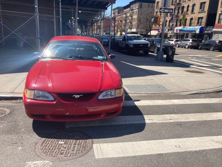 This red car, with an NYPD placard in its dash, parked half on the sidewalk, half in a crosswalk.