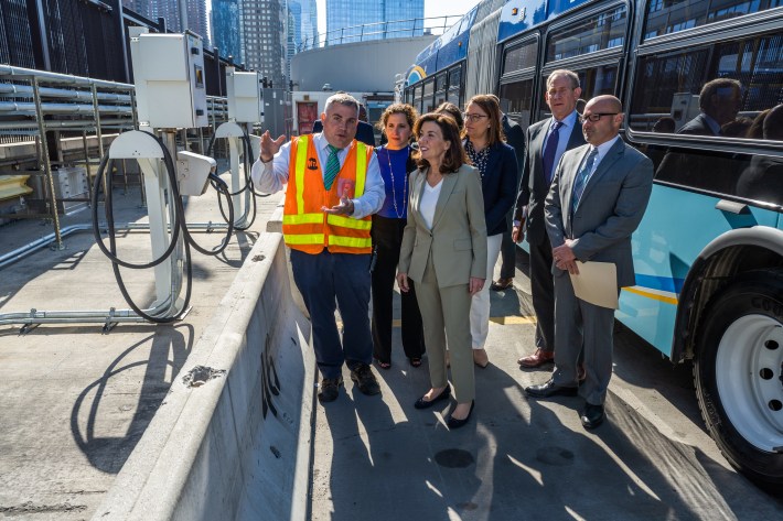 Gov. Hochul (center) and MTA brass discuss electric bus chargers (at left). Photo: MTA