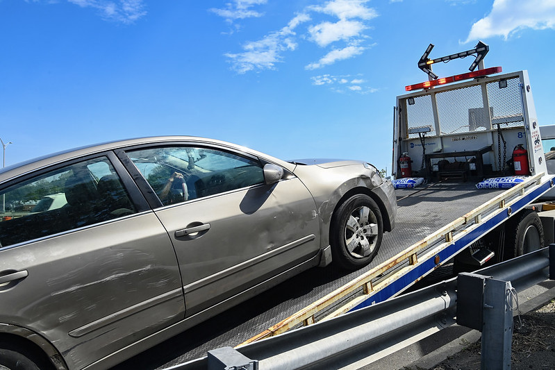 A car with an obscured license plate is towed by the MTA on a sunny day.