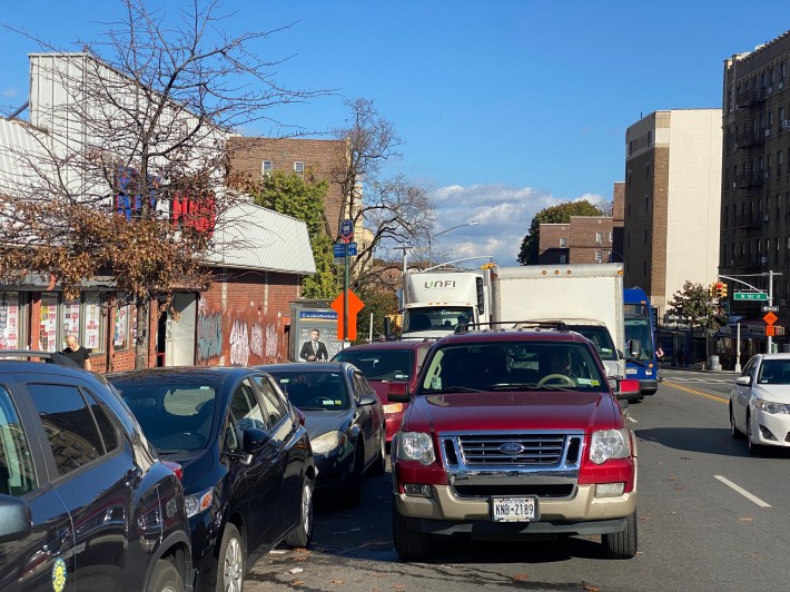 Double-parked cars and trucks block an MTA bus stop on Broadway in Washington Heights and force everyone else to squeeze by. Photo: Kevin Duggan
