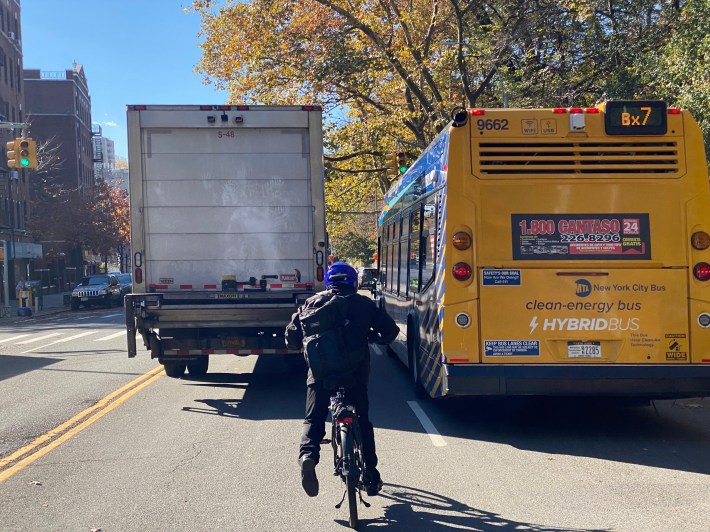 A cyclist fends for space with an MTA bus and a truck on Broadway near Fort Tyron Park. Photo: Kevin Duggan